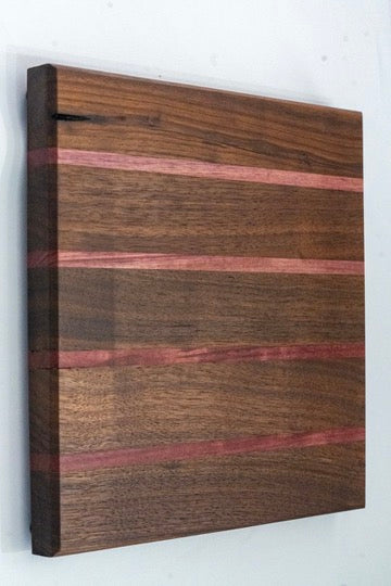 his cutting board features a walnut wood base, accented by four stripes of alternating Padauk (red) wood. The captivating hues you behold are the authentic colors of each wood, untouched by any stains or dyes.